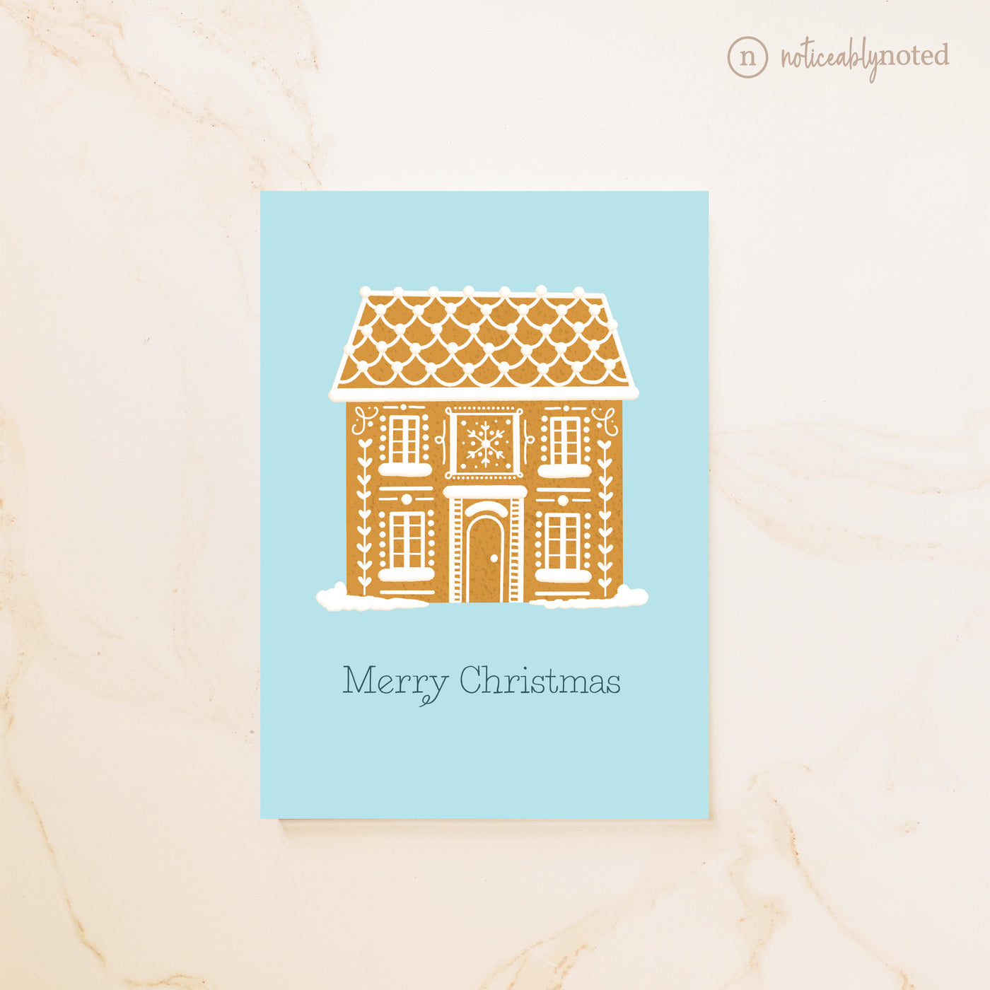 Gingerbread house design on a blue card with 'Merry Christmas' text, on a beige background.