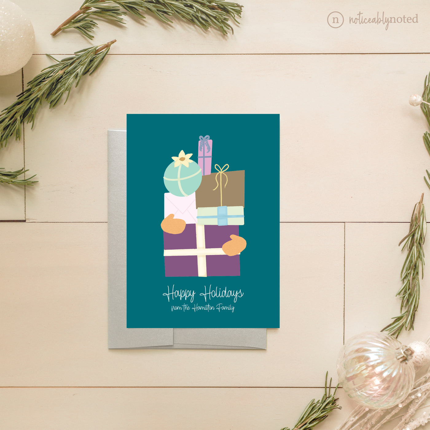 Holiday card with colorful gift boxes on a teal background, surrounded by Christmas decorations.