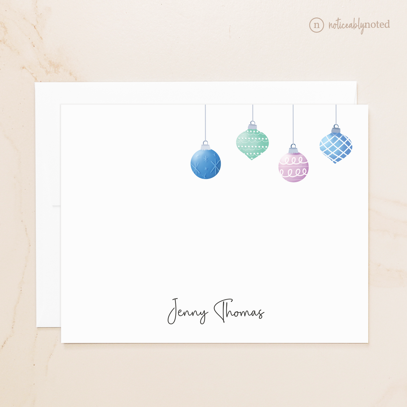 Note card with colorful Christmas ornaments and a name on a beige background