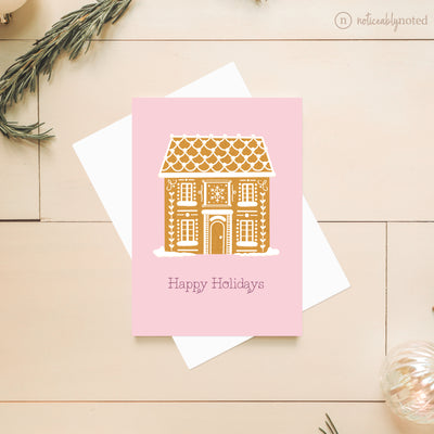 Greeting card with gingerbread house design and 'Happy Holidays' text on a pink background.