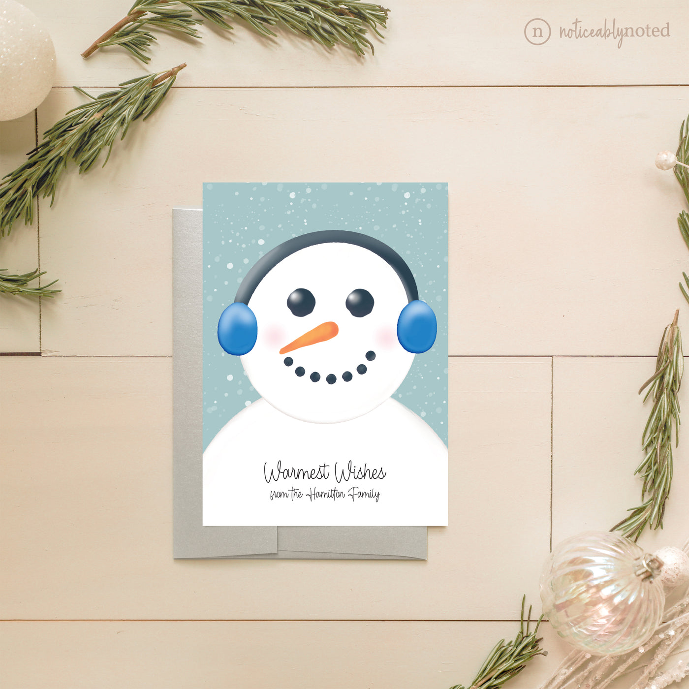 Christmas card with a snowman design on a wooden surface with decorative elements.