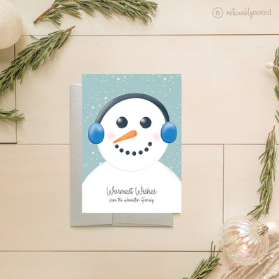 Christmas card with a snowman design on a wooden surface with decorative elements.