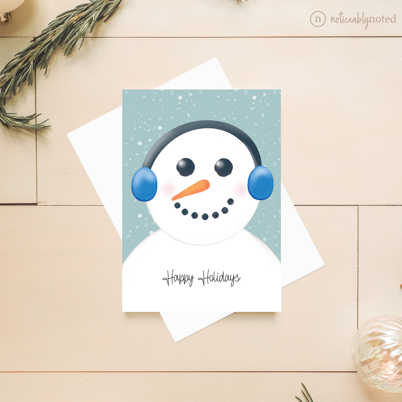 Greeting card with a snowman design and 'Happy Holidays' text on a wooden surface.