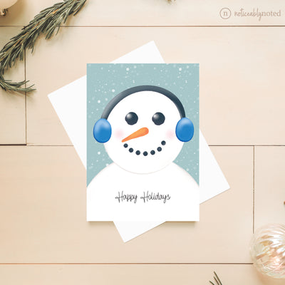 Greeting card with a snowman design and 'Happy Holidays' text on a wooden surface.