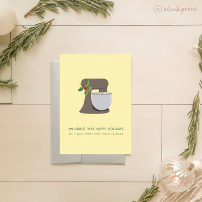 Greeting card with a mixer illustration and holiday message on a light wooden surface.