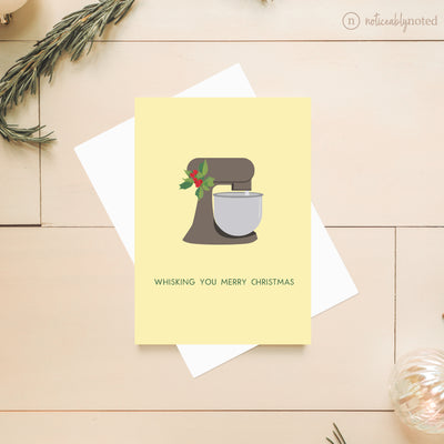 Christmas card with a stand mixer illustration and text on a wooden surface.