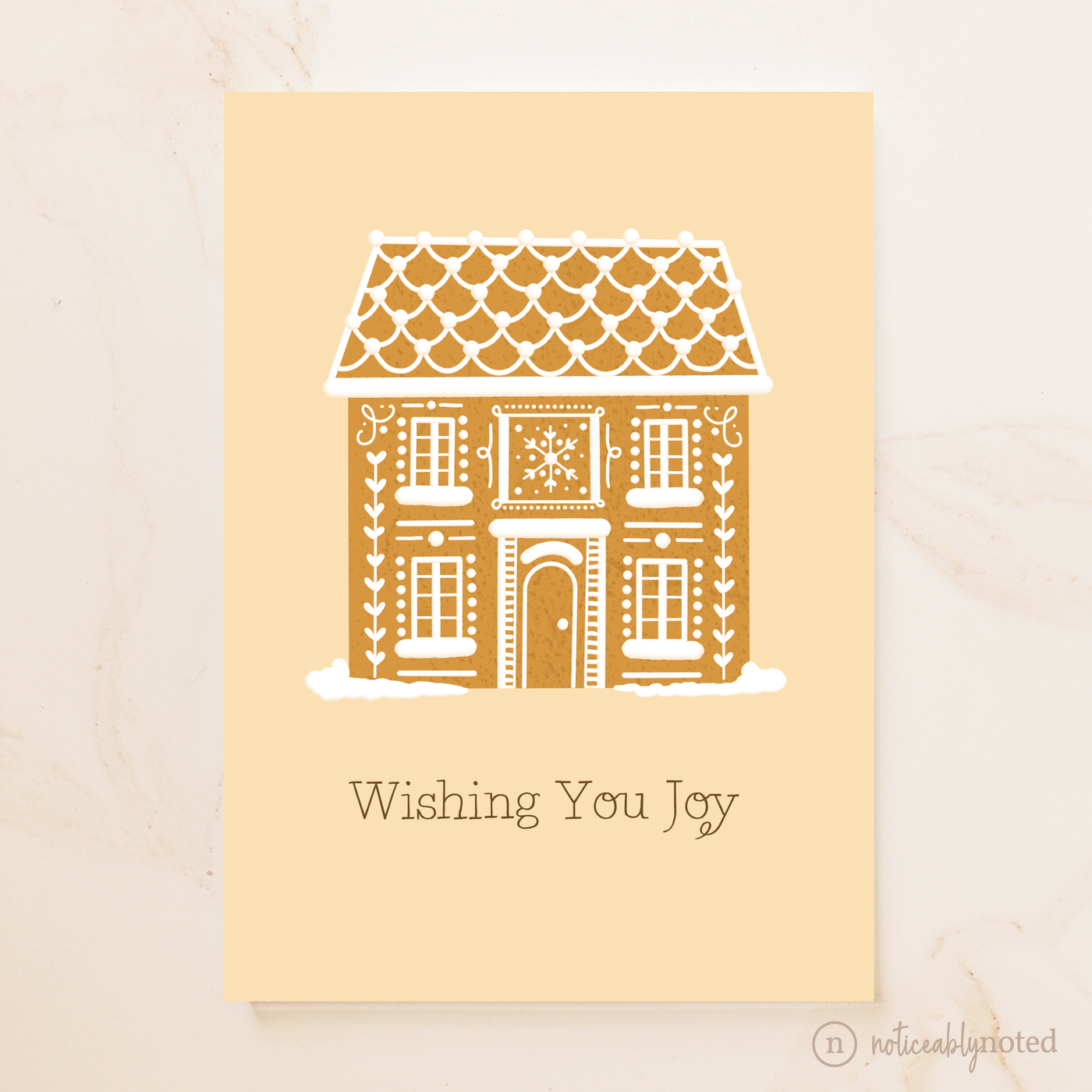 Greeting card with a gingerbread house design and 'Wishing You Joy' text on a beige background.