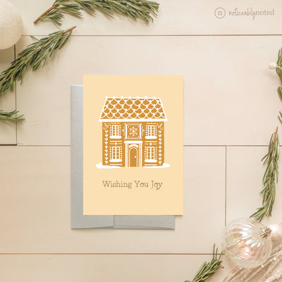 Greeting card with gingerbread house design and 'Wishing You Joy' text, surrounded by decorative elements on a light wooden surface.