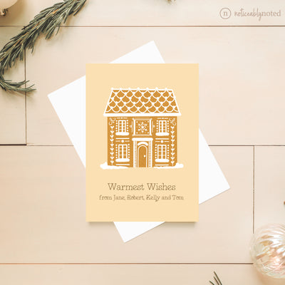 Greeting card with gingerbread house design and 'Warmest Wishes' text on a wooden surface.
